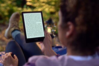 Uma mulher lê um livro no Kindle sentada em um banco ao ar livre.