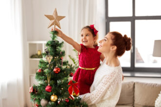 Conceito de família, férias de inverno e pessoas - mãe e filha felizes decorando a árvore de Natal em casa