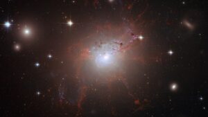 NGC 1275: galáxia de núcleo brilhante, filamentos avermelhados e estrelas com picos de difração sobre fundo escuro.