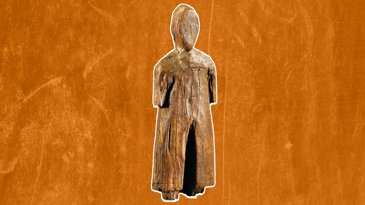 Estatueta de madeira esculpida de figura humana em pé, com braços ao longo do corpo e vestes longas, sobre fundo laranja.