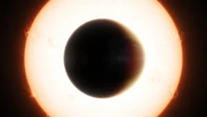 Silhueta escura de um planeta gigante levemente ovalado diante de uma estrela brilhante, com fino halo de luz na borda.